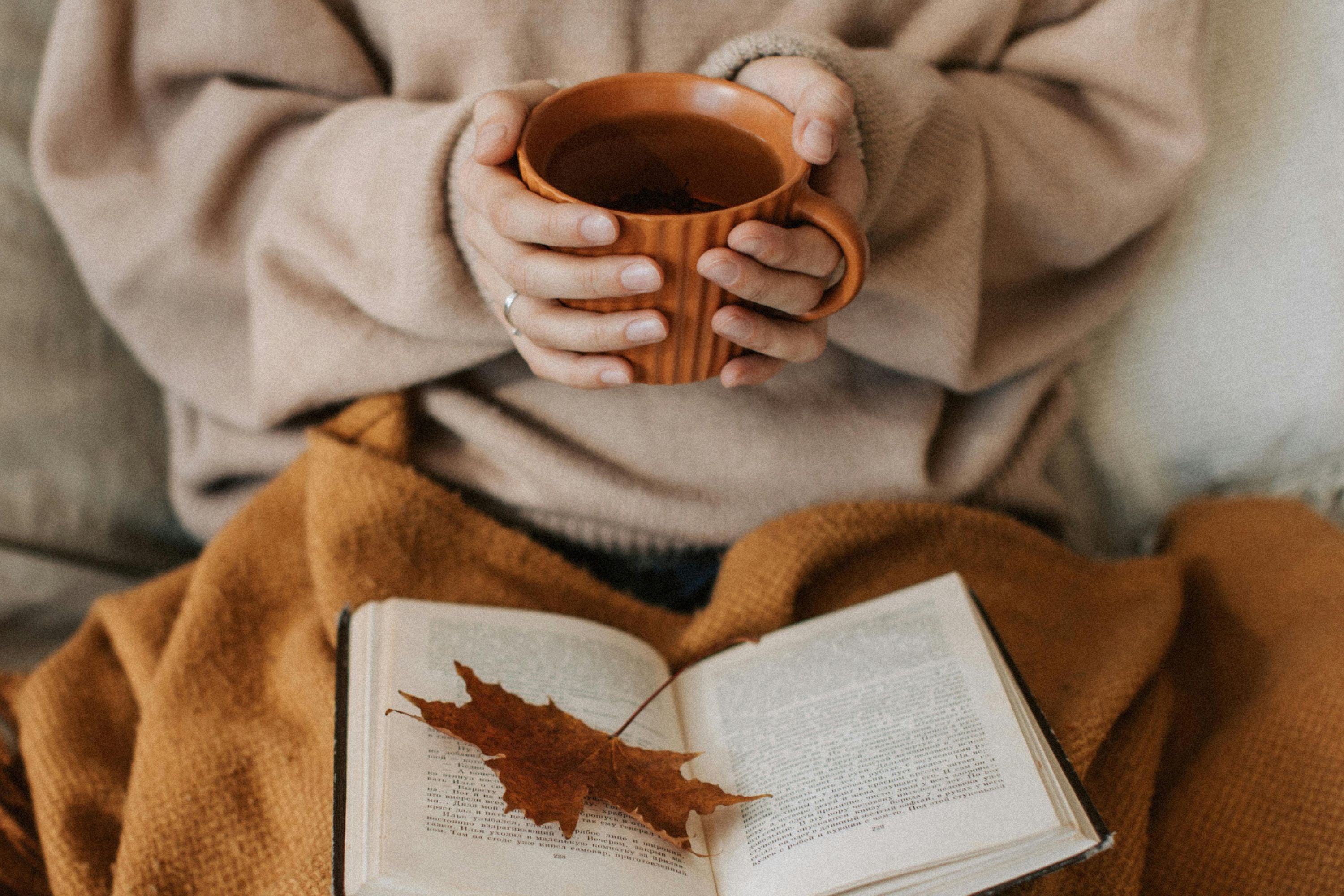 femme assise dans son lit tenant une tasse entre ses mains et avec un livre sur ses genoux